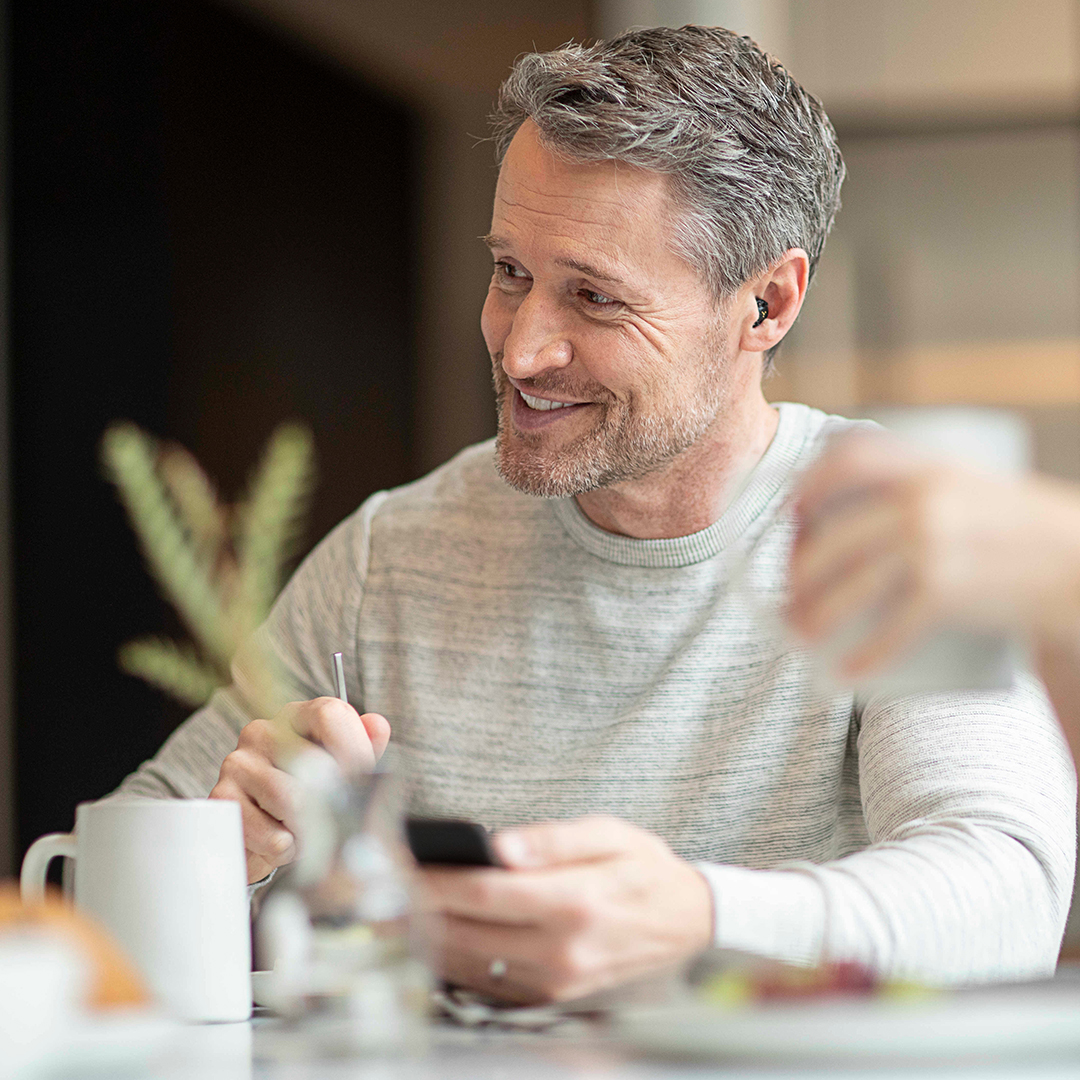 Man smiling using his phone and drinking coffee