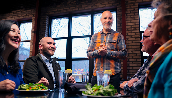 people around a table with salads and water with lemon slices jovially talking